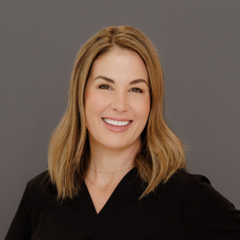 Headshot of woman APRN nurse in black scrubs and grey background